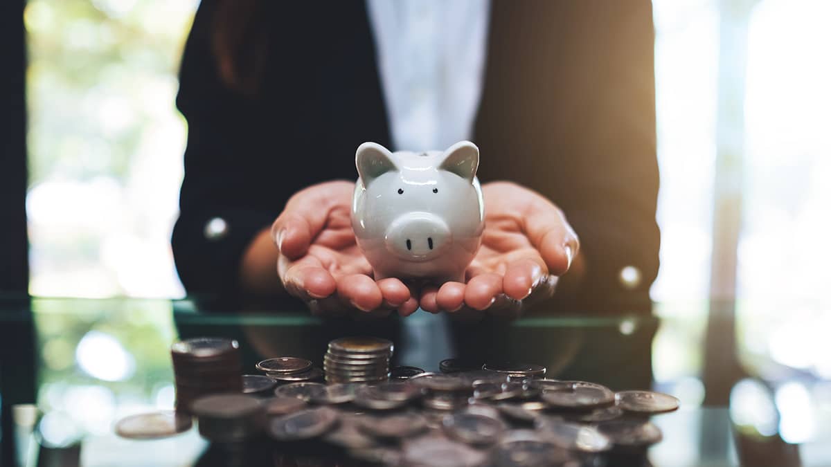 hands holding piggy bank surrounded by coins