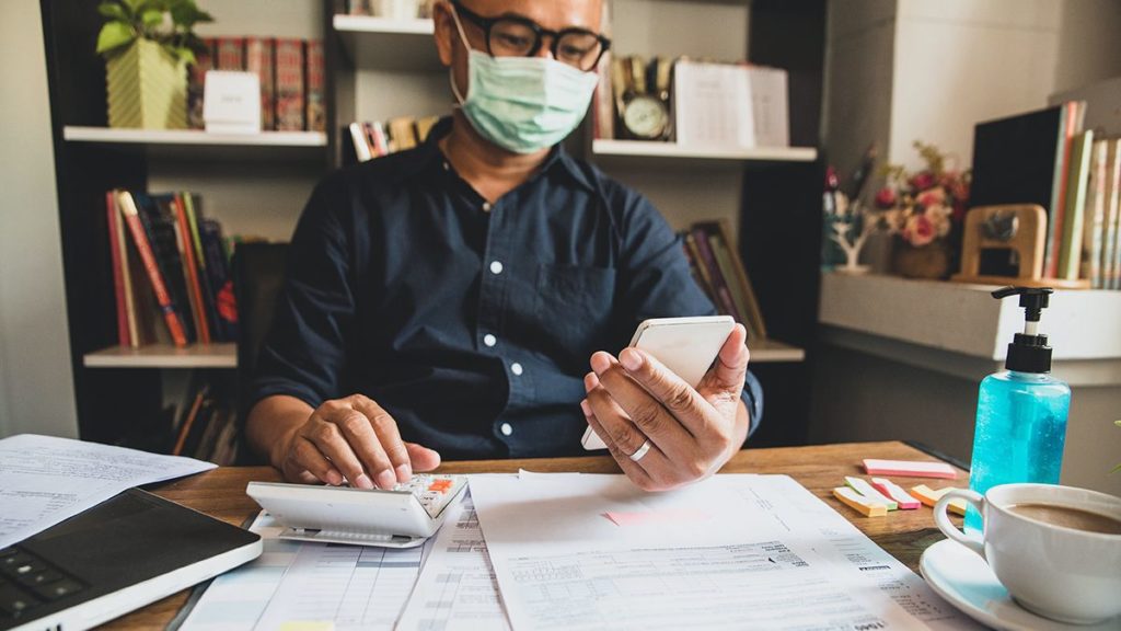 man wearing mask looking at his phone and using a calculator to determine ppp loan forgiveness