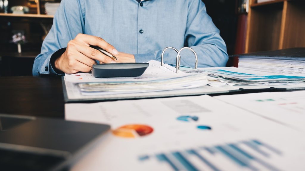 man in blue button down holds pen and works with simple journal entries and charts