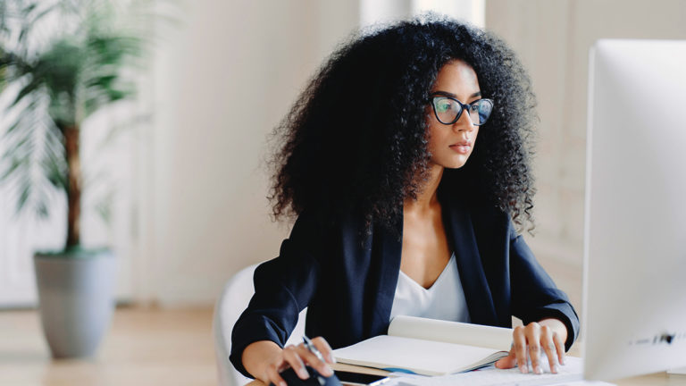 woman wearing glasses using computer and taking notes